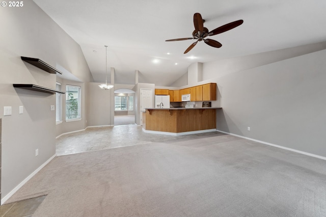 unfurnished living room with ceiling fan with notable chandelier, light colored carpet, and high vaulted ceiling