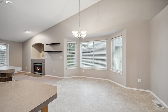 unfurnished living room with a tiled fireplace, a healthy amount of sunlight, light tile patterned floors, and an inviting chandelier