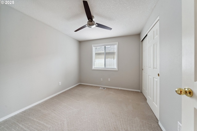 unfurnished bedroom featuring ceiling fan, light carpet, a textured ceiling, and a closet