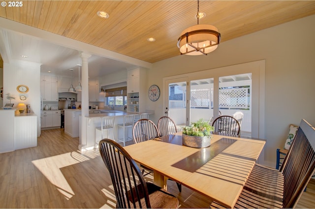 dining area featuring decorative columns, sink, light hardwood / wood-style flooring, and wooden ceiling