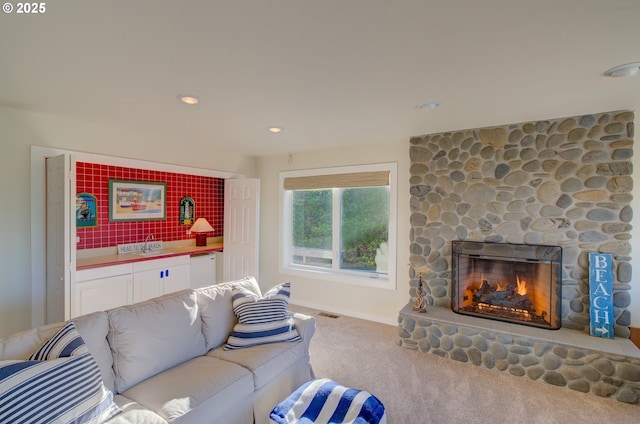 living room with a stone fireplace, sink, and light colored carpet