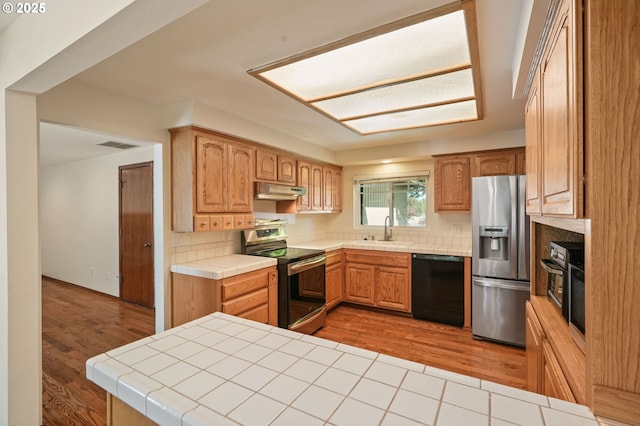 kitchen featuring stainless steel appliances, a sink, tile countertops, and light wood-type flooring