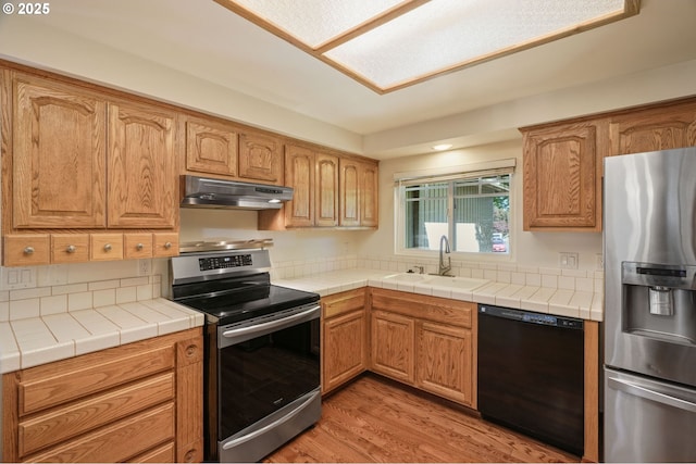 kitchen featuring stainless steel appliances, under cabinet range hood, a sink, and light wood-style floors