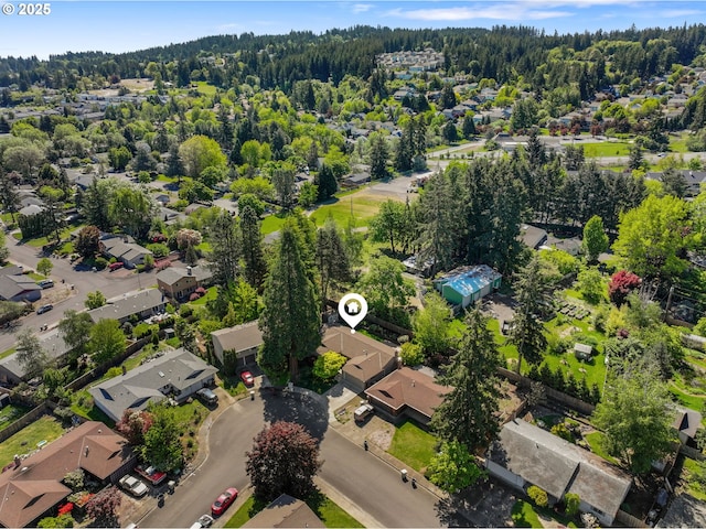 aerial view of property and surrounding area with nearby suburban area and a heavily wooded area