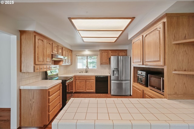 kitchen with appliances with stainless steel finishes, under cabinet range hood, tile countertops, a sink, and decorative backsplash
