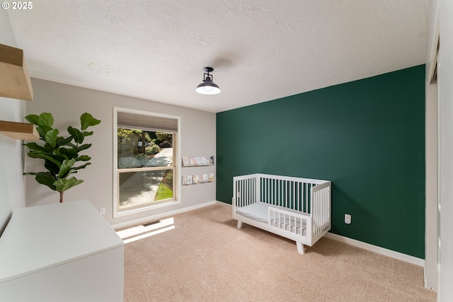unfurnished bedroom with carpet flooring, a textured ceiling, a crib, and baseboards