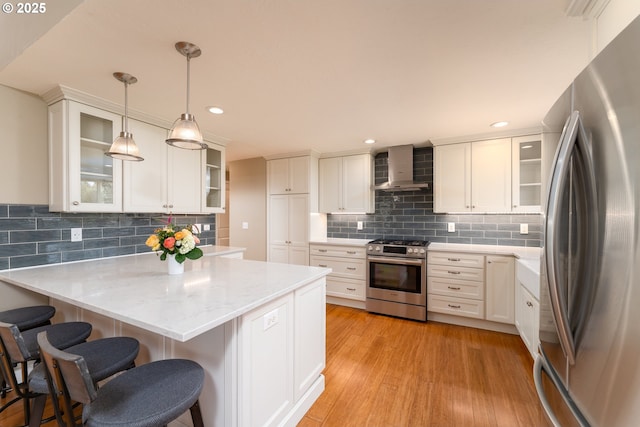 kitchen featuring tasteful backsplash, wall chimney exhaust hood, stainless steel appliances, a peninsula, and a kitchen bar