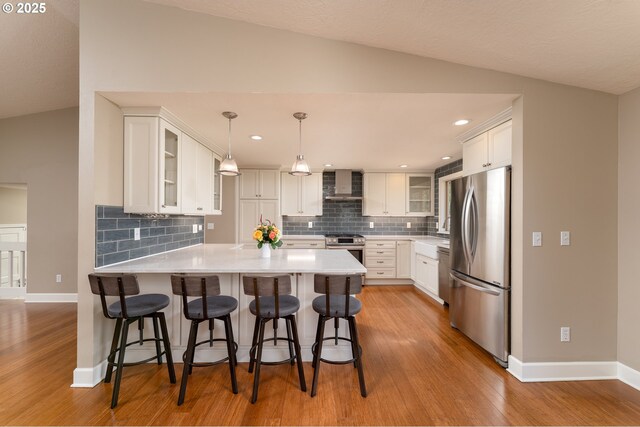 kitchen featuring light wood-style flooring, wall chimney exhaust hood, stainless steel appliances, a peninsula, and lofted ceiling
