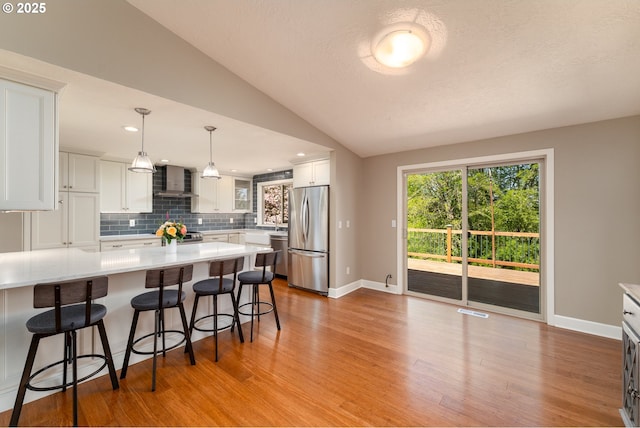 kitchen with wall chimney range hood, decorative backsplash, appliances with stainless steel finishes, light countertops, and a breakfast bar