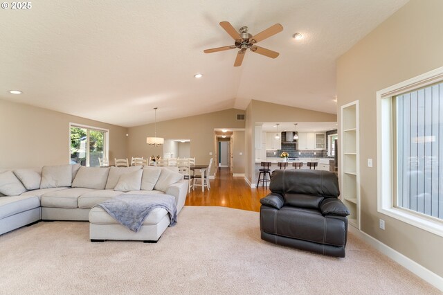 living room featuring baseboards, a ceiling fan, light colored carpet, and lofted ceiling