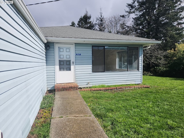 doorway to property with roof with shingles and a yard