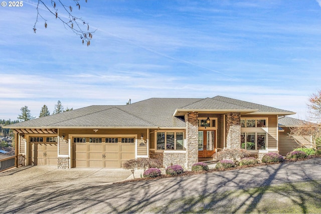 prairie-style home with an attached garage, french doors, stone siding, and driveway