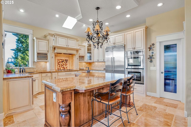 kitchen with a chandelier, cream cabinetry, stone tile floors, and appliances with stainless steel finishes