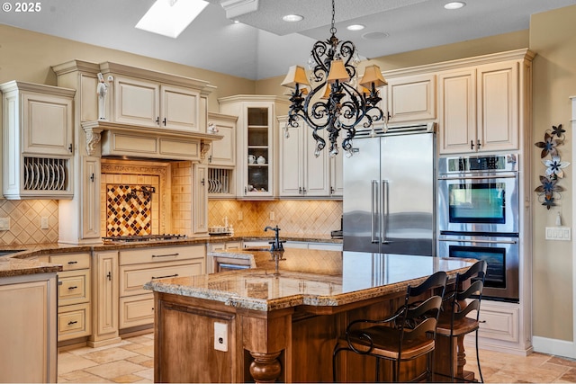 kitchen featuring light stone counters, a sink, cream cabinets, stone tile floors, and stainless steel appliances