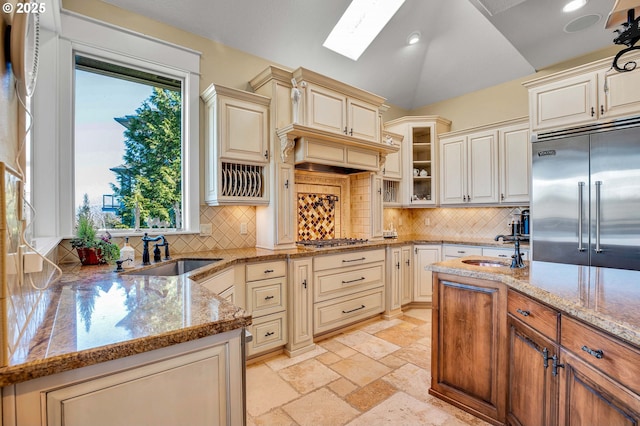 kitchen with a sink, light stone countertops, cream cabinets, and appliances with stainless steel finishes