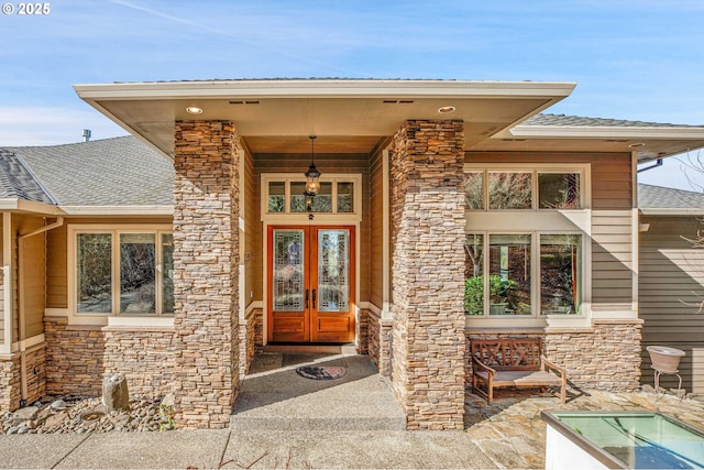 property entrance with stone siding, french doors, and a shingled roof