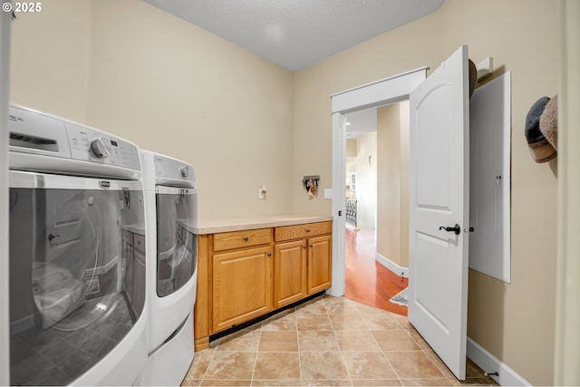 washroom featuring baseboards, cabinet space, a textured ceiling, and independent washer and dryer