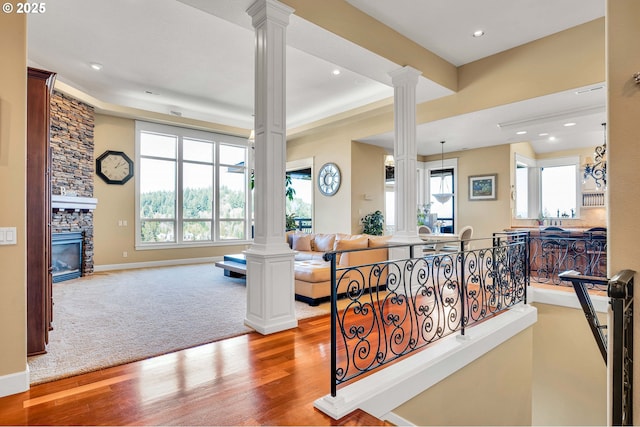 carpeted living area featuring wood finished floors, baseboards, decorative columns, a fireplace, and recessed lighting