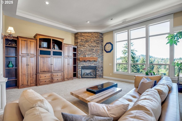 living room featuring baseboards, light carpet, a raised ceiling, and a stone fireplace