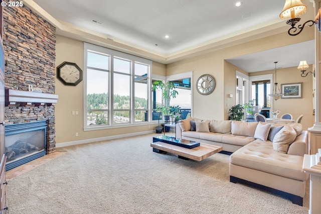 living room featuring visible vents, a stone fireplace, an inviting chandelier, carpet flooring, and baseboards