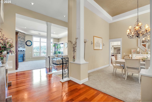 dining room with baseboards, a tray ceiling, a fireplace, wood finished floors, and ornate columns