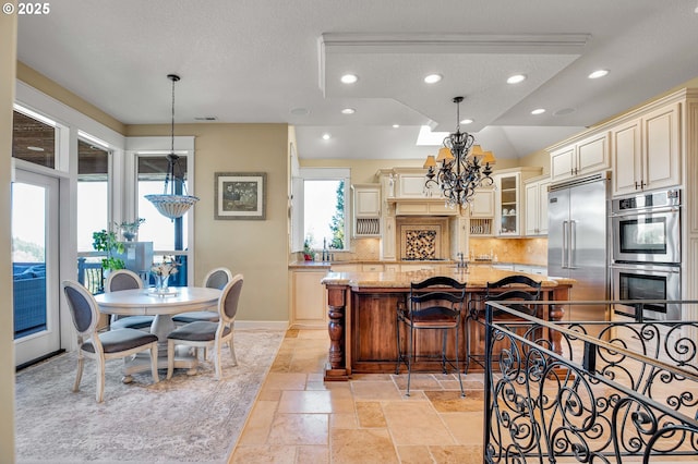 kitchen with light stone countertops, stone tile flooring, decorative backsplash, cream cabinetry, and appliances with stainless steel finishes