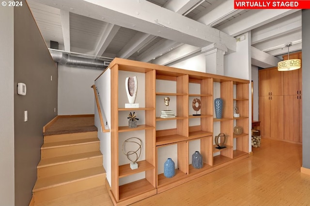 staircase featuring wood finished floors, beam ceiling, and baseboards