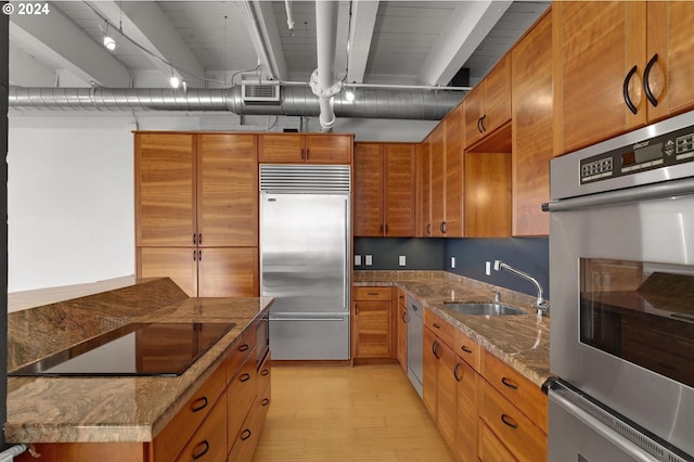 kitchen with stainless steel appliances, a sink, brown cabinets, and dark stone counters