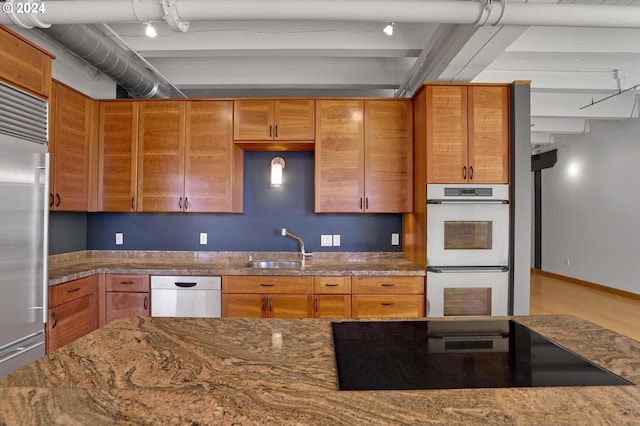 kitchen featuring appliances with stainless steel finishes, a sink, dark stone counters, beamed ceiling, and brown cabinets