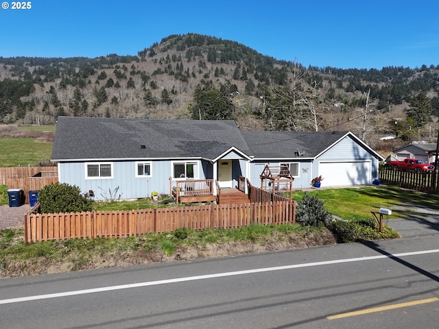 ranch-style home featuring a fenced front yard, a mountain view, an attached garage, and roof with shingles