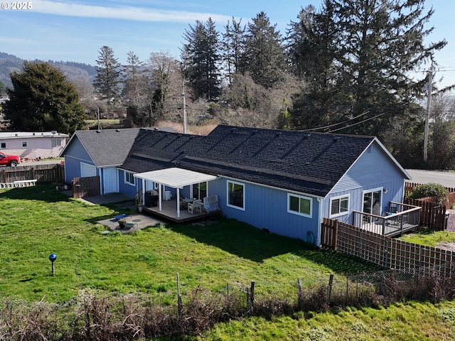 rear view of house featuring a yard, a shingled roof, a deck, and fence