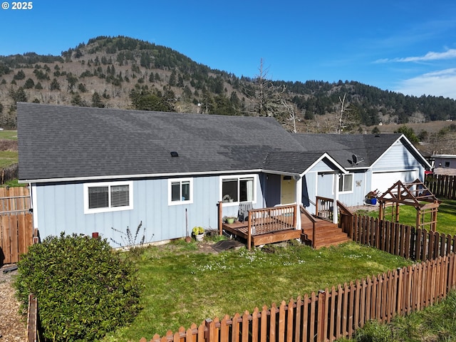 view of front facade featuring a deck with mountain view, a front lawn, fence, board and batten siding, and a shingled roof