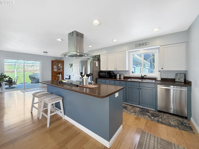 kitchen with a sink, a kitchen breakfast bar, dark countertops, stainless steel appliances, and island range hood