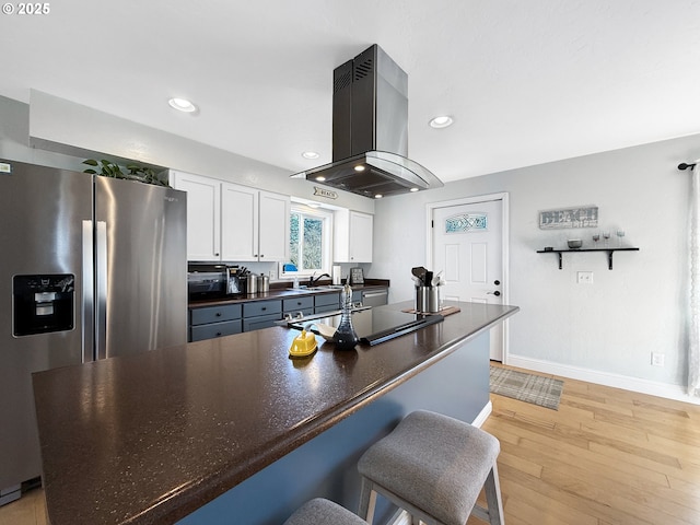 kitchen with stainless steel refrigerator with ice dispenser, island exhaust hood, dark countertops, white cabinetry, and light wood-style floors