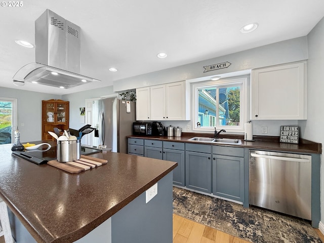 kitchen with a sink, dark countertops, white cabinetry, appliances with stainless steel finishes, and exhaust hood