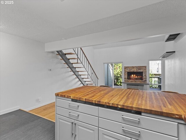 kitchen featuring a stone fireplace, dark wood-type flooring, baseboards, wood counters, and open floor plan