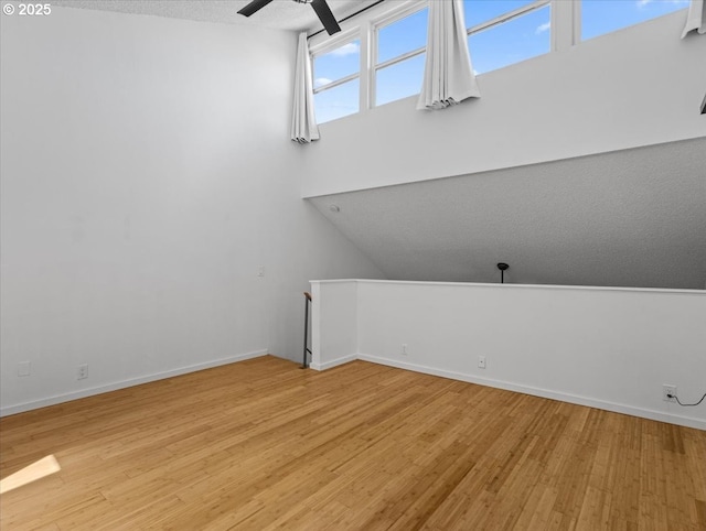bonus room with light wood-style floors, a textured ceiling, baseboards, and ceiling fan