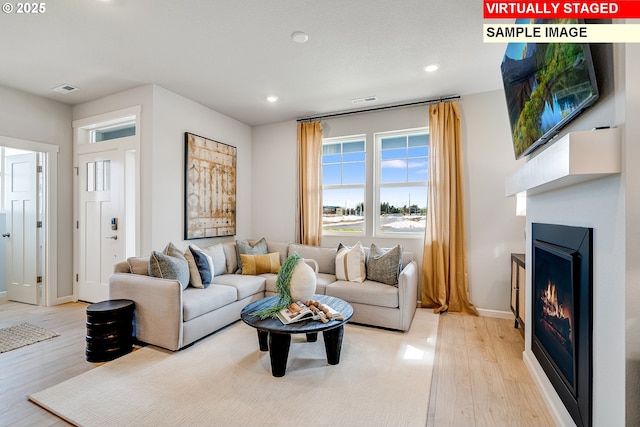 living area featuring light wood-style floors, a lit fireplace, visible vents, and recessed lighting