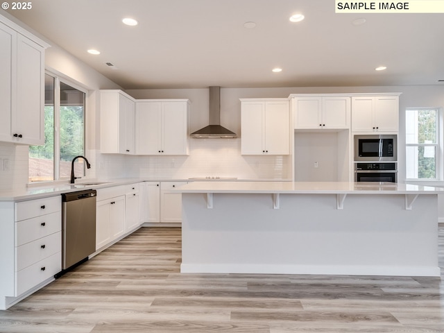 kitchen with white cabinetry, a kitchen island, stainless steel appliances, and wall chimney range hood