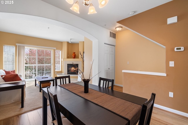 dining room featuring visible vents, light wood finished floors, arched walkways, a warm lit fireplace, and a chandelier