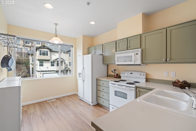 kitchen with a sink, white appliances, light wood-style floors, and green cabinetry