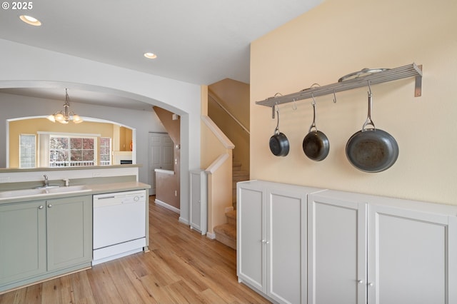 kitchen with light wood finished floors, arched walkways, white dishwasher, a sink, and light countertops