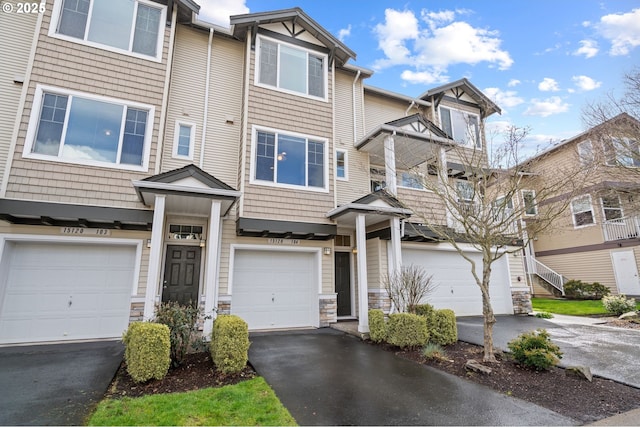 townhome / multi-family property featuring an attached garage, stone siding, and driveway