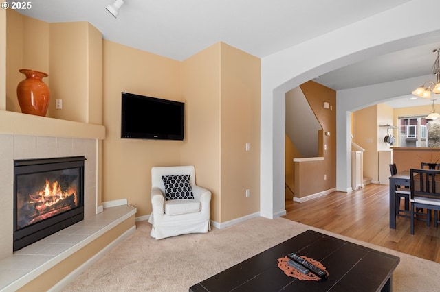 living room with arched walkways, a tile fireplace, carpet, and baseboards