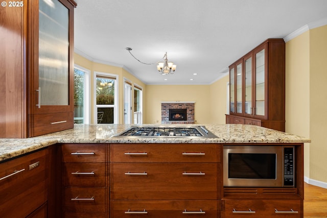 kitchen featuring crown molding, glass insert cabinets, light stone countertops, and appliances with stainless steel finishes