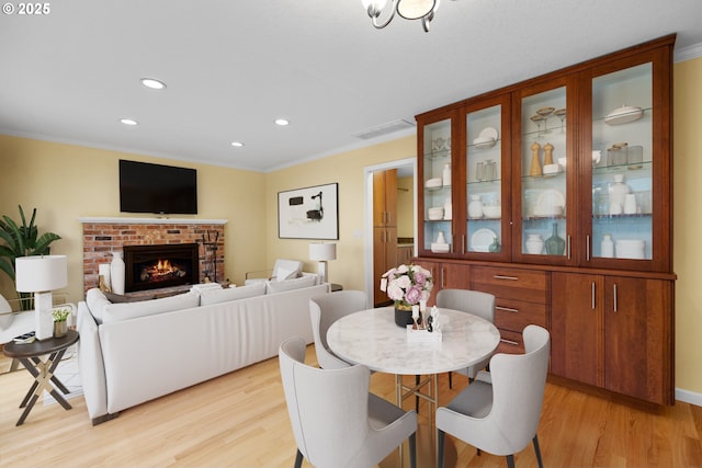 dining room with visible vents, light wood-style floors, a fireplace, and crown molding