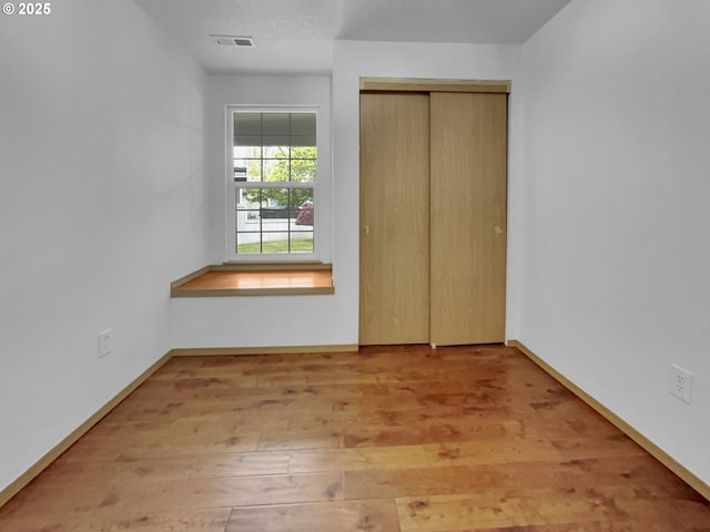 unfurnished bedroom with baseboards, a closet, wood finished floors, and visible vents