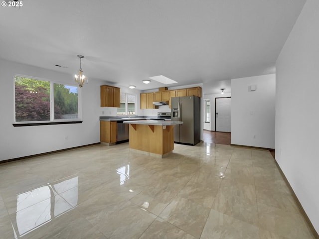 kitchen with a kitchen island, appliances with stainless steel finishes, baseboards, marble finish floor, and under cabinet range hood