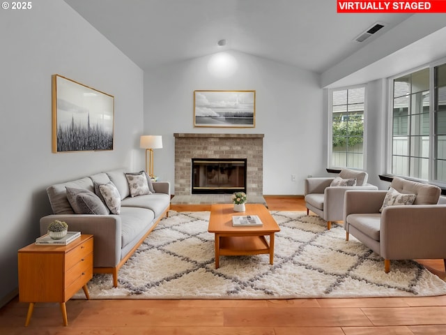 living room featuring visible vents, wood finished floors, vaulted ceiling, and a fireplace