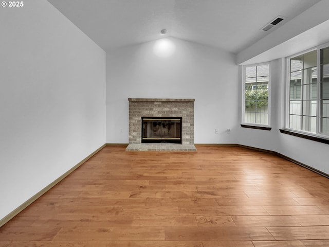 unfurnished living room featuring visible vents, wood finished floors, a fireplace, baseboards, and vaulted ceiling
